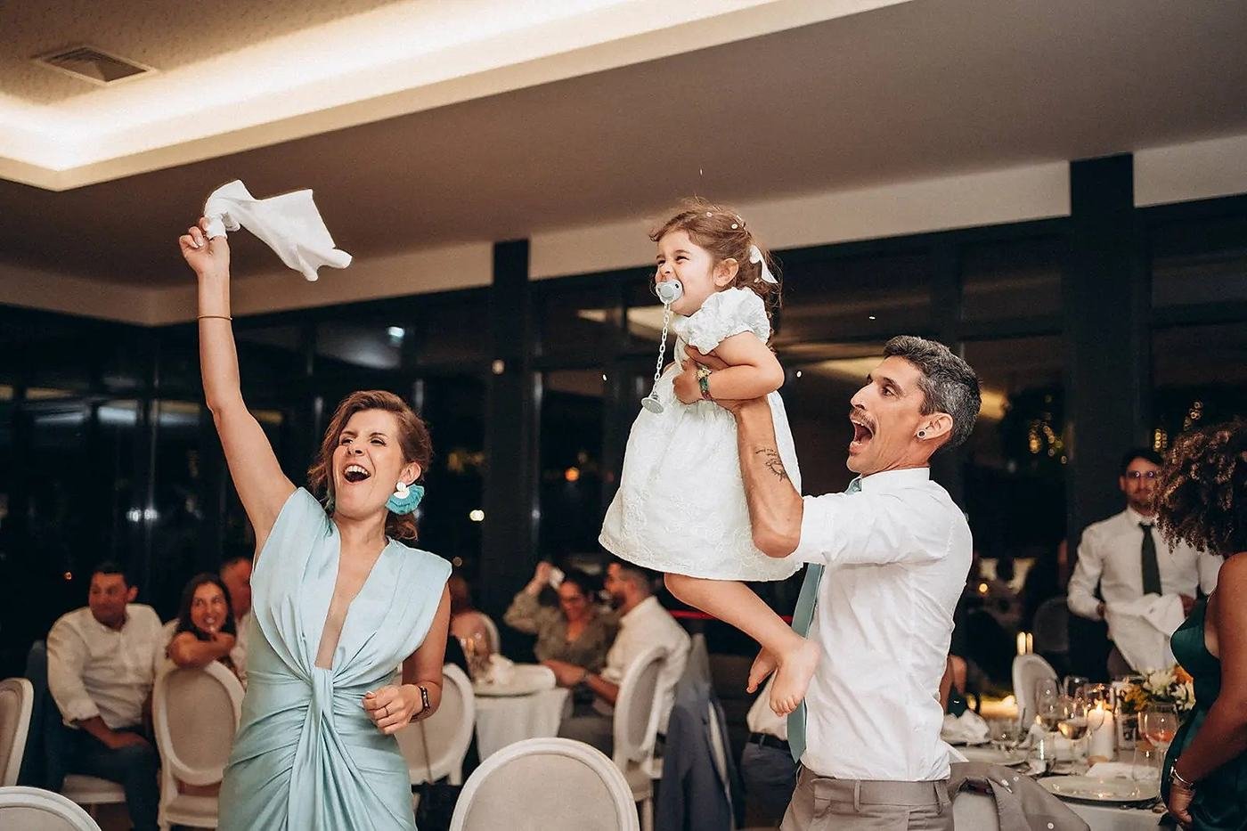 Batizado animado: criança ao colo, guardanapo no ar e a sala inteira a festejar