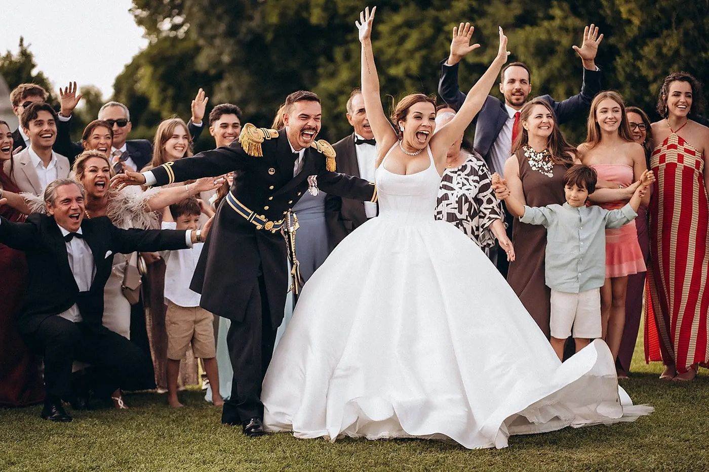 Noivos e convidados a festejar no jardim, todos de braços no ar