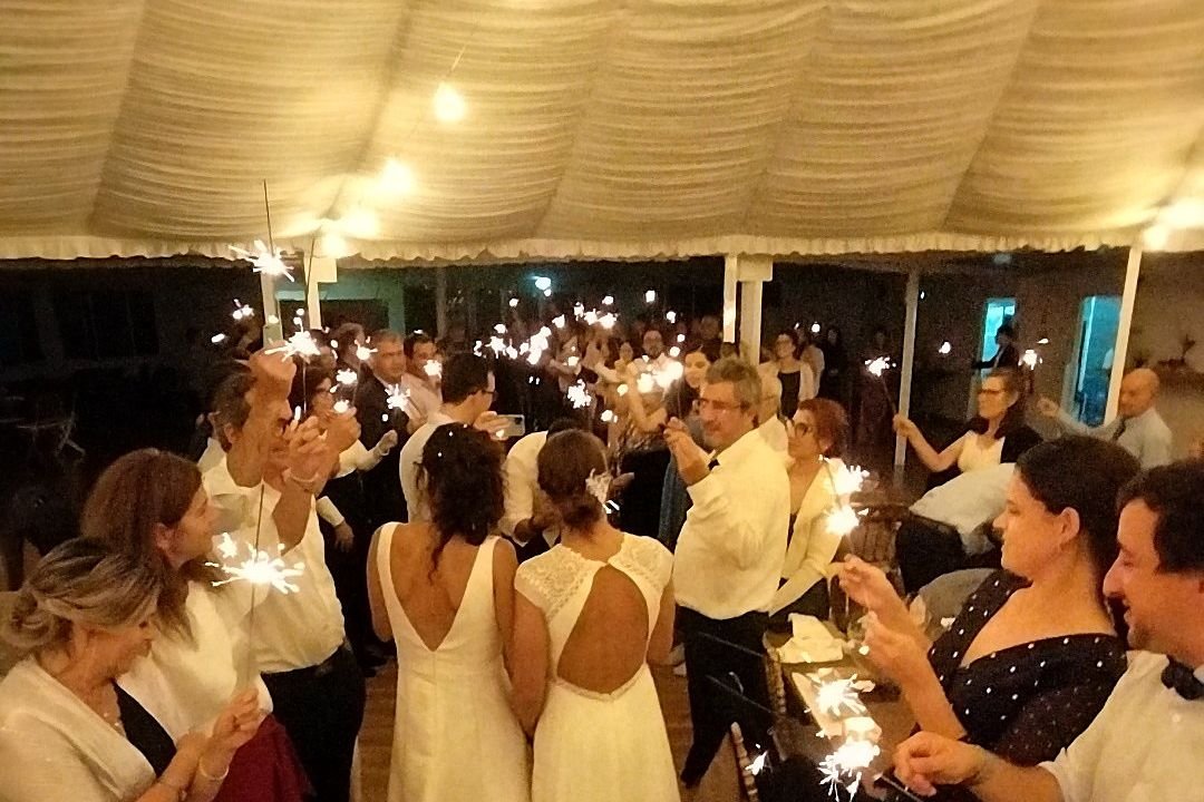 As noivas de mãos dadas no meio dos convidados, com faíscas acesas à volta