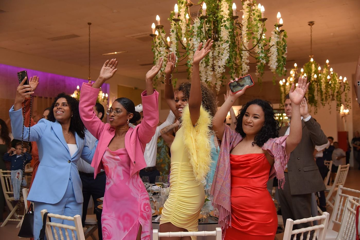 Convidadas de braços no ar numa festa de casamento com família brasileira e africana